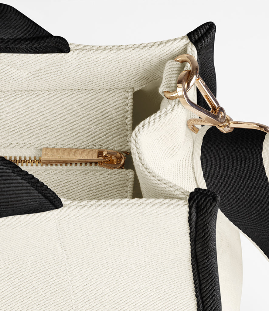 Close-up of a white handbag with black accents and gold hardware on a light gray background